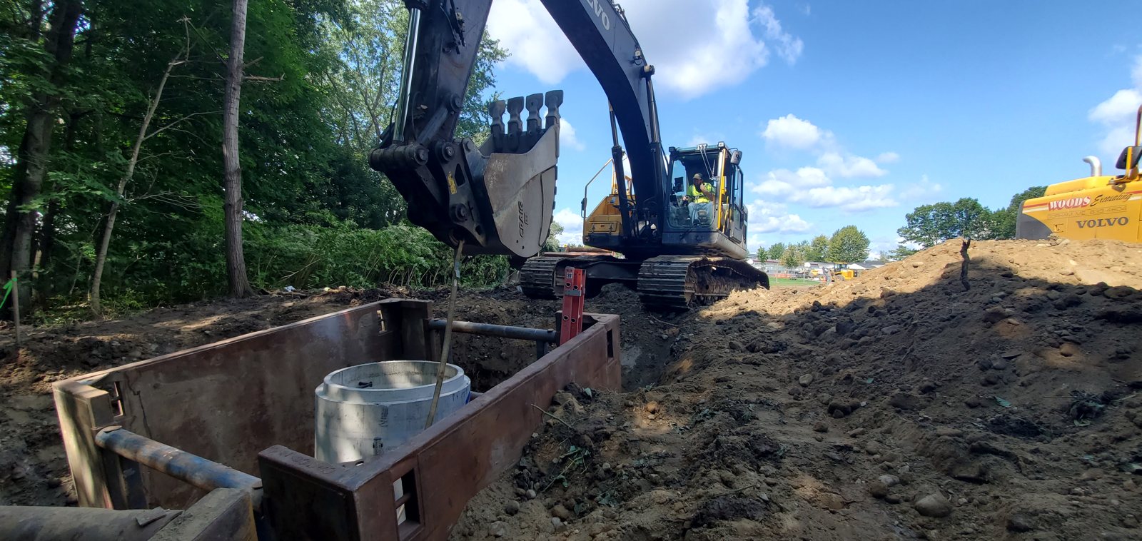 Woods excavator setting a precast structure inside a trench box